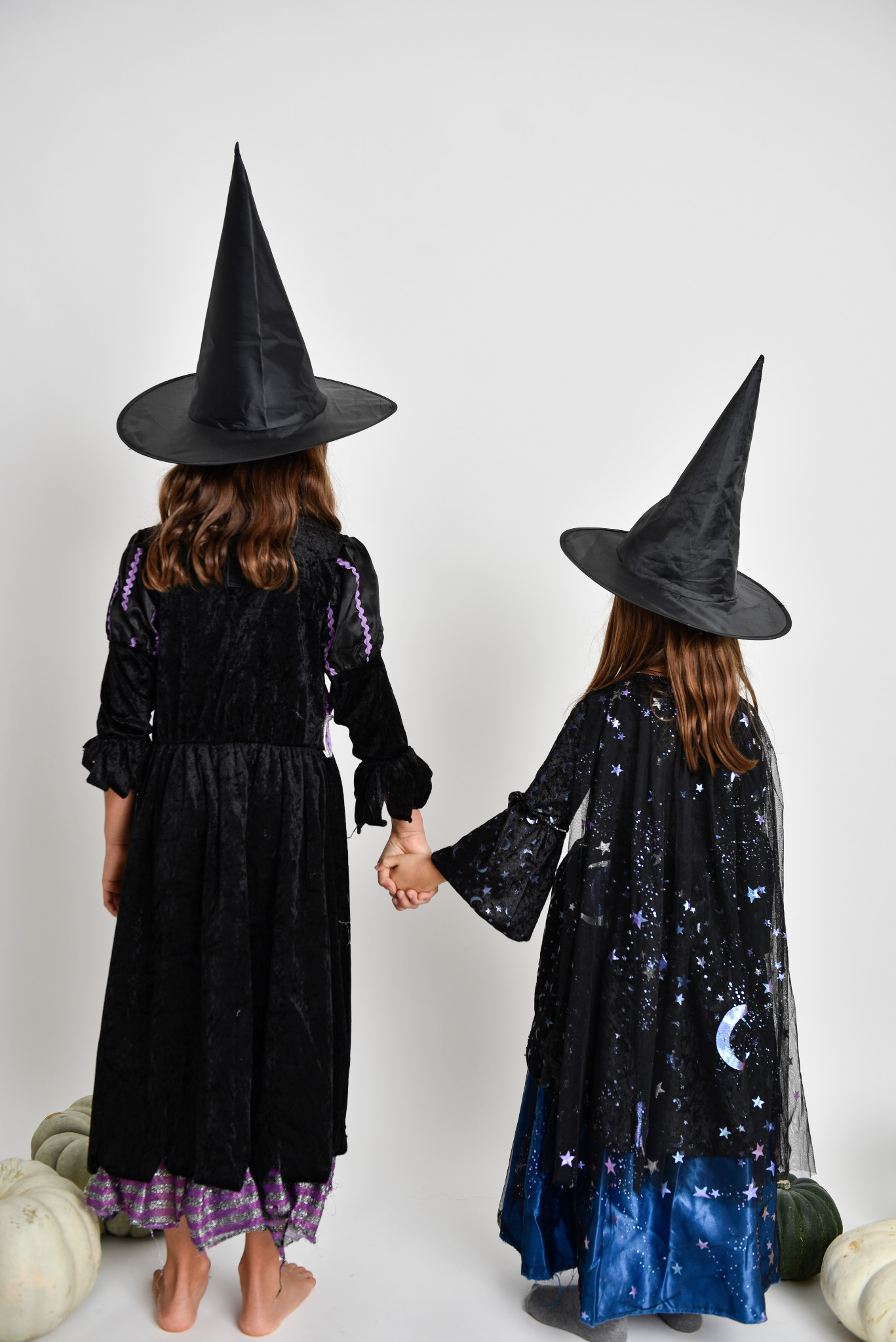 Two children in witch costumes holding hands, photographed from behind in the studio